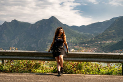 Woman looking away while standing by railing against mountains