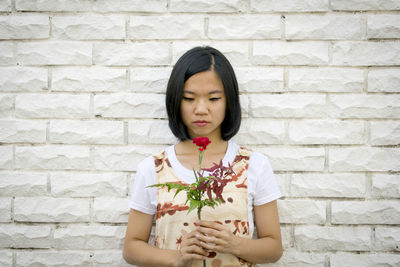 Portrait of young woman holding rose against wall