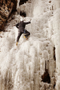 Man climbing frozen waterfall against rock formation