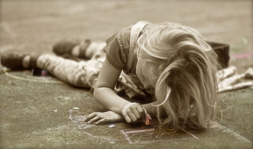 Full length of girl chalk drawing while lying on footpath