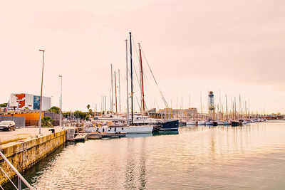 Sailboats moored at harbor against sky during sunset