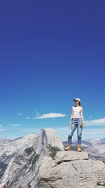 Full length of woman standing on rock against blue sky