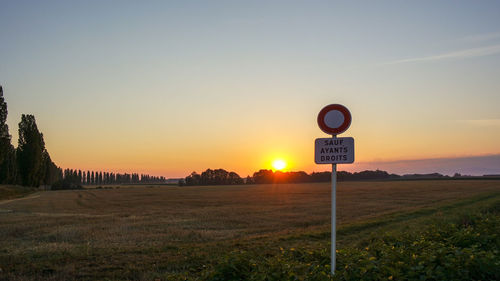 Road sign on field against sky during sunset