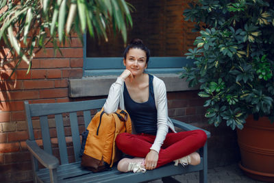 Portrait of smiling young woman sitting on chair against plants