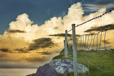 Barbed wire fence against cloudy sky