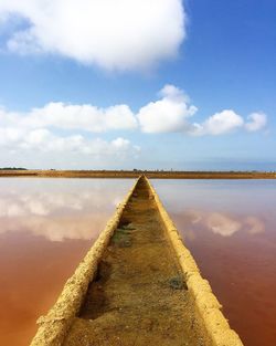 Empty walkway amidst salt lakes against sky