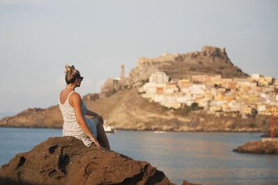 Man standing on rock by sea against clear sky