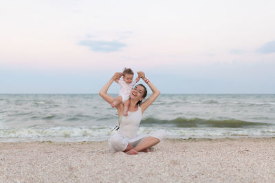 Portrait of smiling mother with daughter sitting against sea