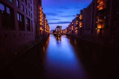 People walking on illuminated canal amidst buildings in city at dusk