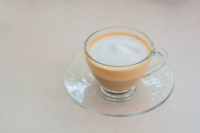 Top view of hot cappuccino coffee and milk froth in clear cup on wooden table in coffee shop.