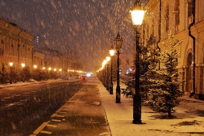 Row of illuminated lamp posts by street during snowfall