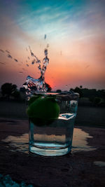 Close-up of water splashing in glass against sky at sunset