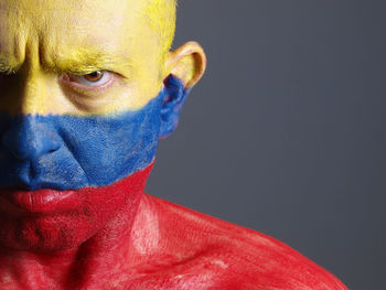 Close-up portrait of angry man with venezuelan flag body paint against gray background
