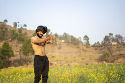 Shirtless man standing on field against sky