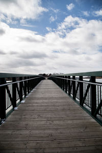 Wooden footbridge on pier against sky