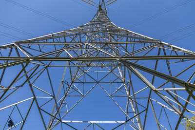 Low angle view of electricity pylon against clear blue sky