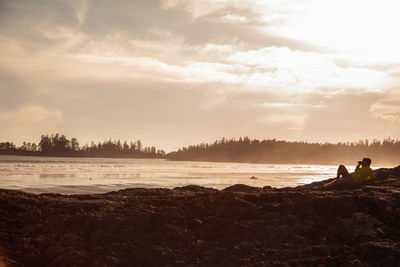 Man relaxing at beach against sky during sunset