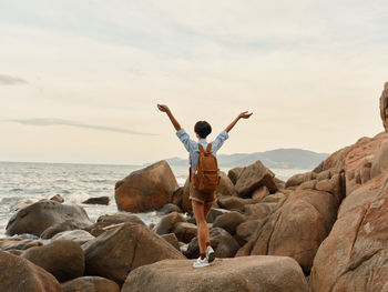 Rear view of man with arms raised standing on rock at beach