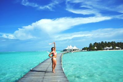 Woman wearing bra and panty standing amidst sea on pier during sunny day