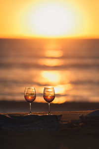 Close-up of wineglass on beach against sky during sunset