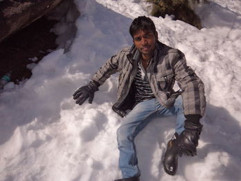 Portrait of young man sitting on snowcapped field