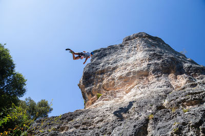 Low angle view of man rock climbing against clear blue sky
