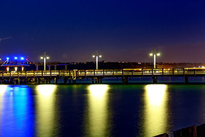 Illuminated bridge over river against sky at night