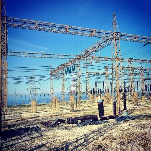 blue, clear sky, fuel and power generation, electricity pylon, power line, electricity, connection, power supply, built structure, sky, sunlight, technology, low angle view, day, cable, outdoors, field, no people, architecture, metal