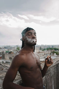 Portrait of young man looking at city against sky