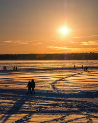 Silhouette people on beach against sky during sunset