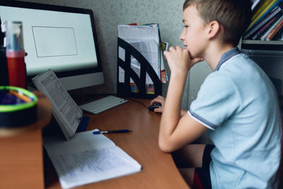 Rear view of boy using mobile phone on table