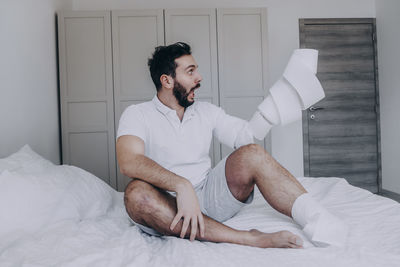 Young man looking away while sitting on bed at home