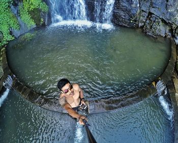 High angle view of young man taking selfie against waterfall