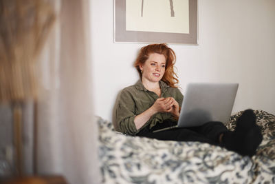 Smiling woman using laptop on bed