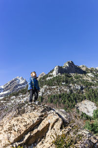 Boy standing on rock against clear blue sky
