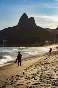 People on beach against mountain range