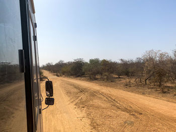 Car on dirt road amidst field against clear sky