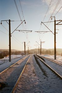 Diminishing perspective of snow covered railroad tracks against sky during sunset