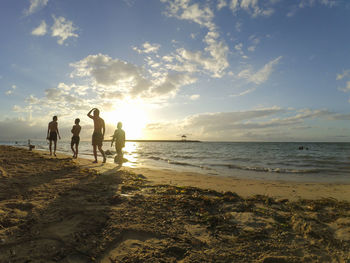 People at beach against sky during sunset