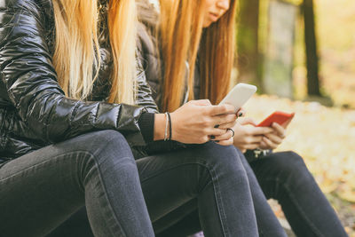 Two girls sitting in the park use smartphone. teen using mobile phone. sisters chat with friends.