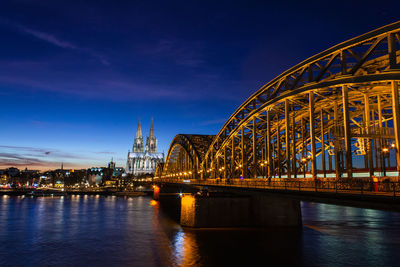 Illuminated bridge over river at sunset