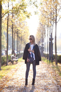 Full length of young woman standing on street during autumn
