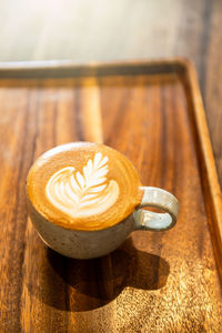 Coffee in ceramic cup on wooden table in cafe with lighting background.