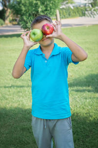 Funny boy covered his eyes with apples. vertical shot.