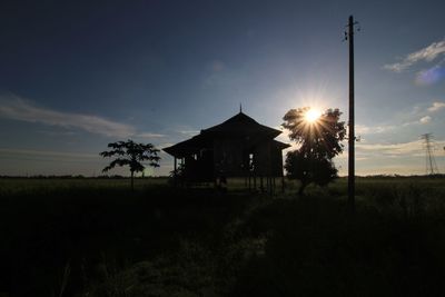 Silhouette building on field against sky at sunset