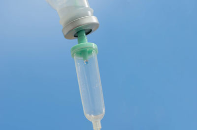 Low angle view of liquid dripping in syringe against blue background