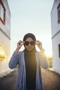 Young woman wearing sunglasses standing against built structure