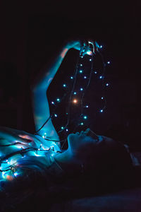 Woman holding illuminated light while lying on bed