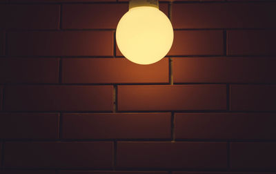 Illuminated light bulb against brick wall