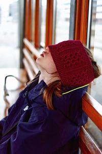 Side view of girl wearing warm clothing while napping against window